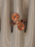 Copper 1 adjustable wire ring, front view showing two spiral ends and copper colored wirework on a white jewelry display.
