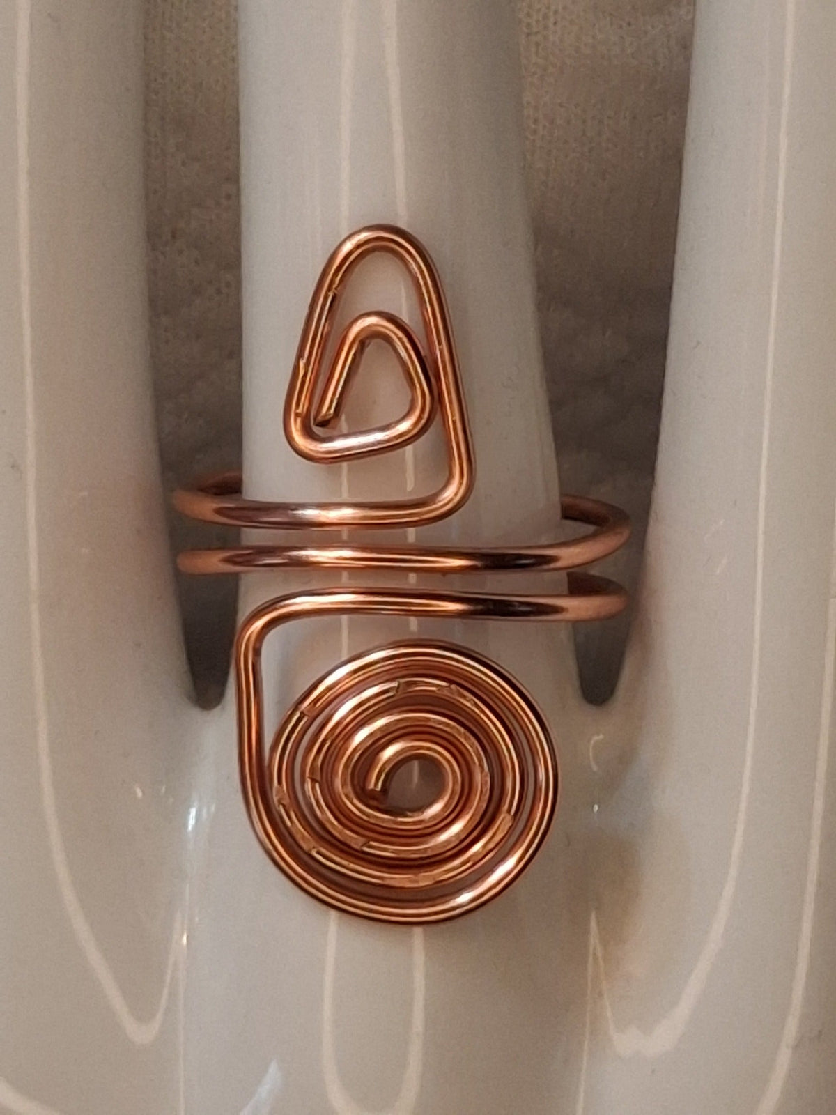 Copper adjustable wire ring 2 with a triangular curl and a large round spiral on a white jewelry display.