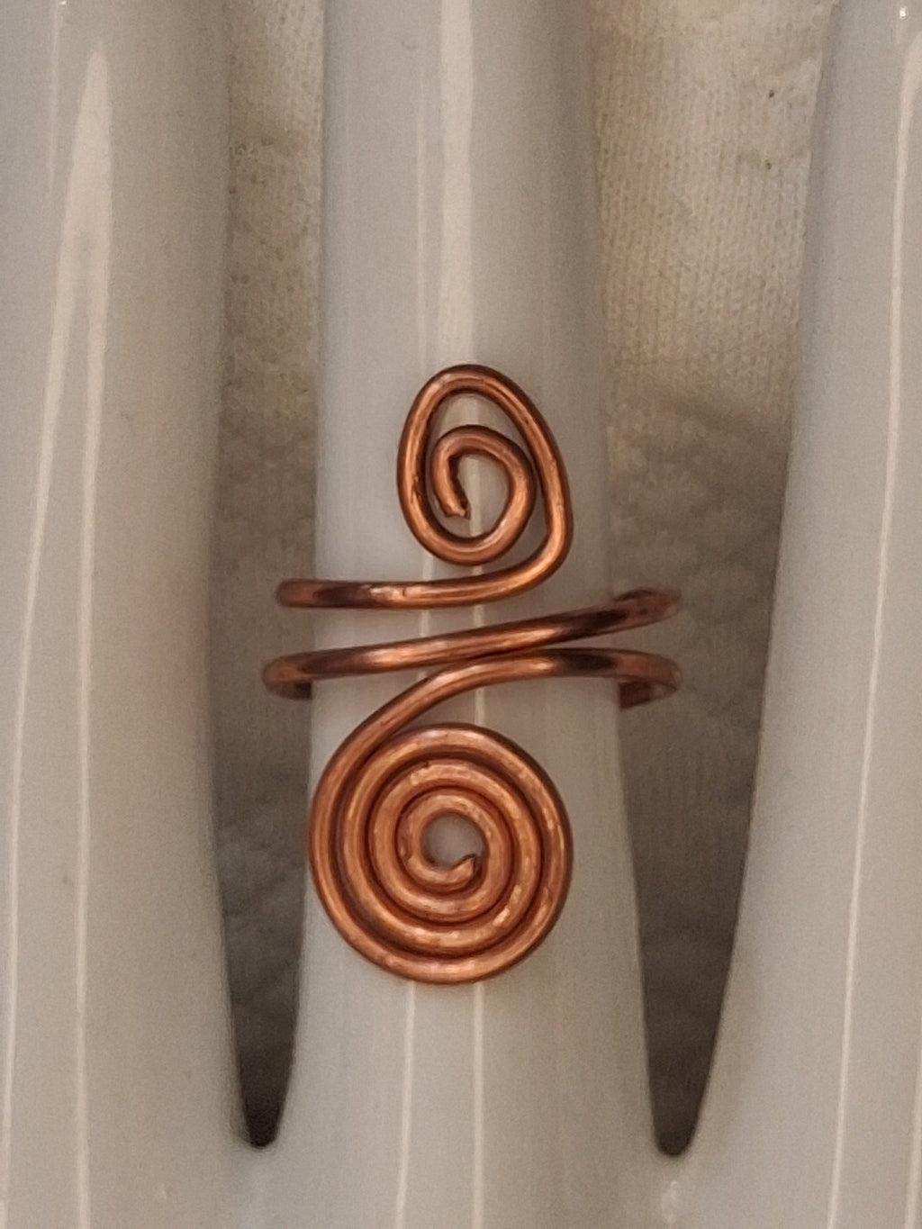 Copper adjustable wire ring 3 with a small oval curl and a larger round spiral on a white jewelry display.