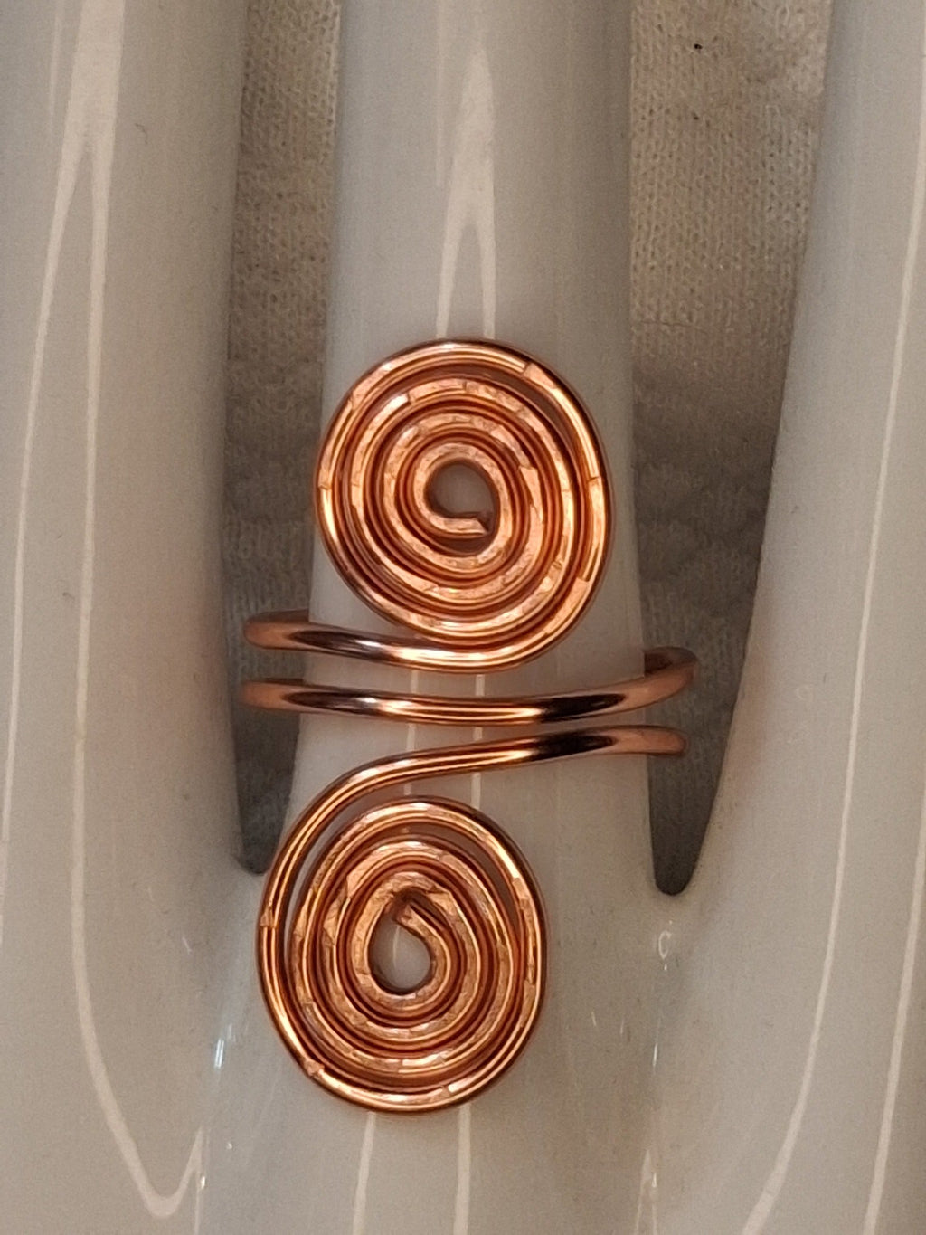 Copper adjustable wire ring 4 with two large spiral ends on a white jewelry display.