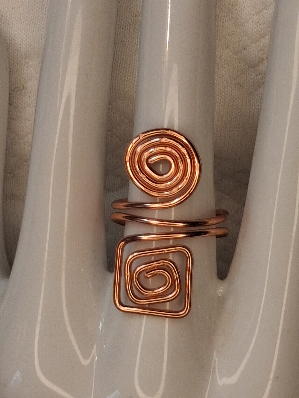 Copper adjustable wire ring 6 with a round spiral and a square spiral on a white jewelry display.
