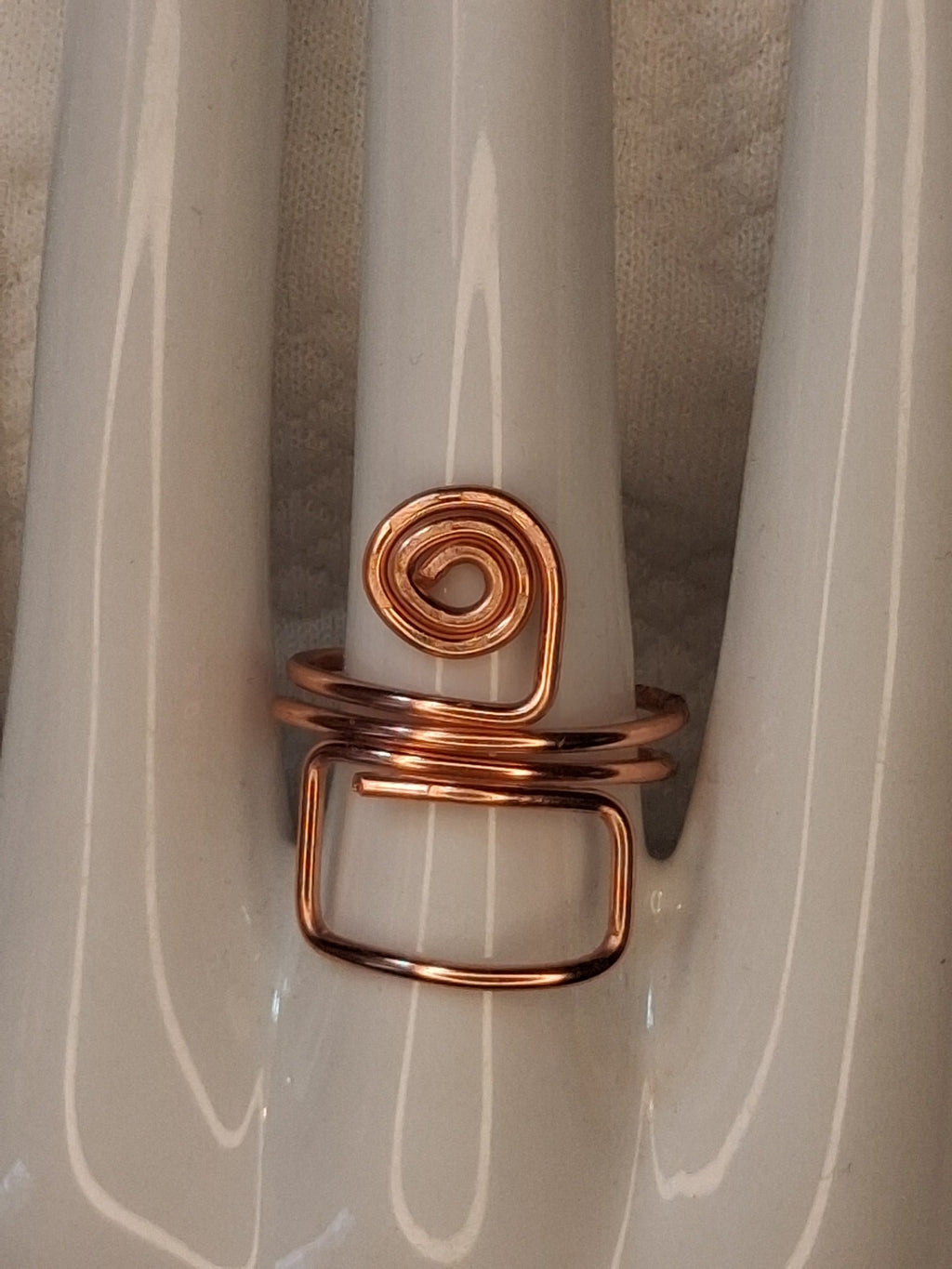 Copper adjustable wire ring 7 with a round spiral and an open rectangular loop on a white jewelry display.