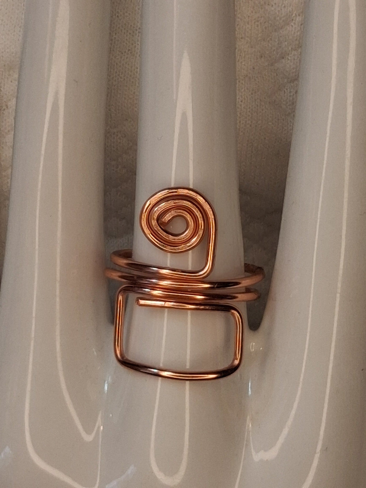 Copper adjustable wire ring 7 with a round spiral and an open rectangular loop on a white jewelry display.