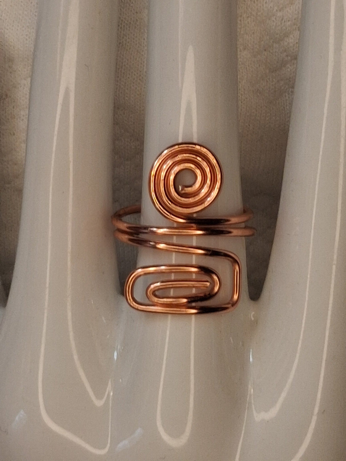 Copper adjustable wire ring 8 with a round spiral and an elongated rectangular curl on a white jewelry display.