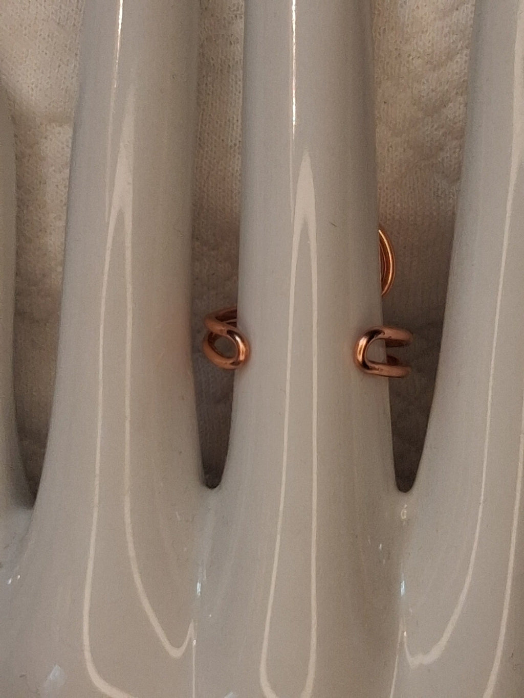 Shared back view showing the open adjustable band and rounded wire ends of a copper colored wire ring on a white jewelry display.