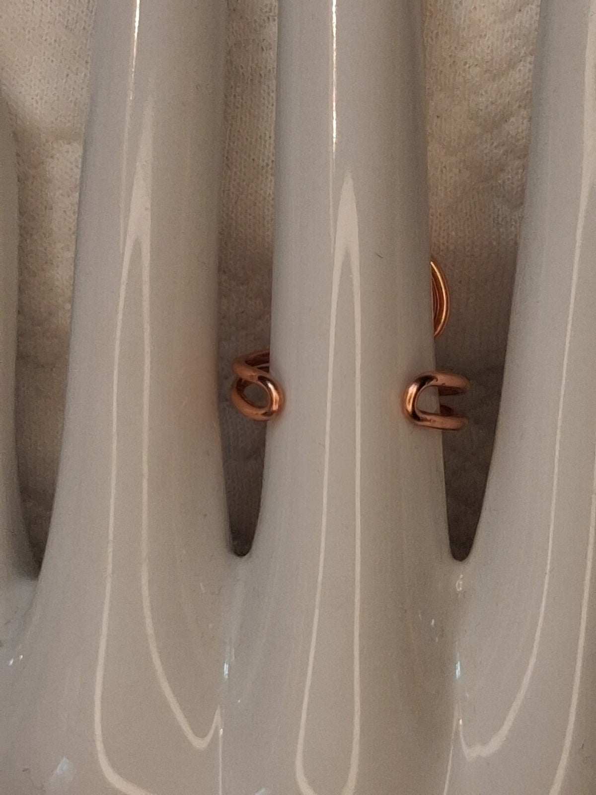 Shared back view showing the open adjustable band and rounded wire ends of a copper colored wire ring on a white jewelry display.