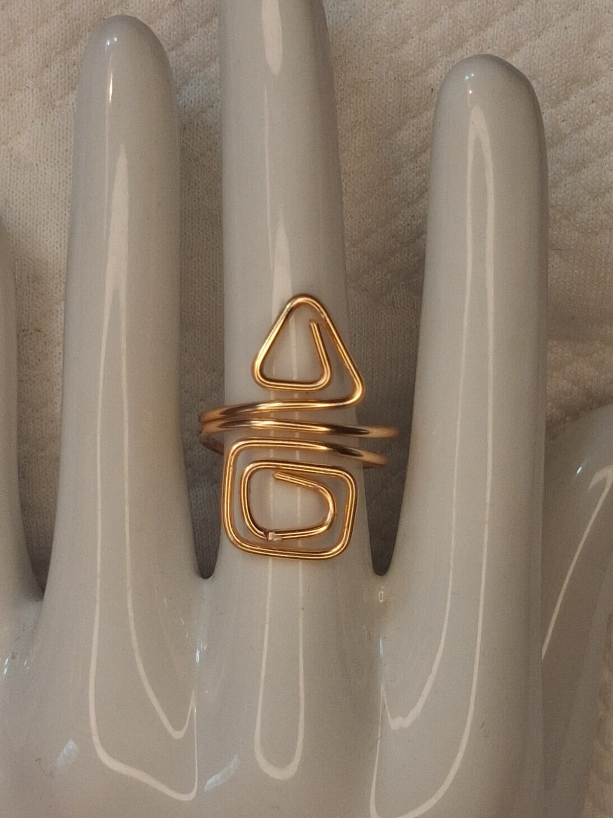 Gold 2 adjustable wire ring with a triangular curl above a rounded rectangular spiral, displayed on a white ceramic jewelry hand.