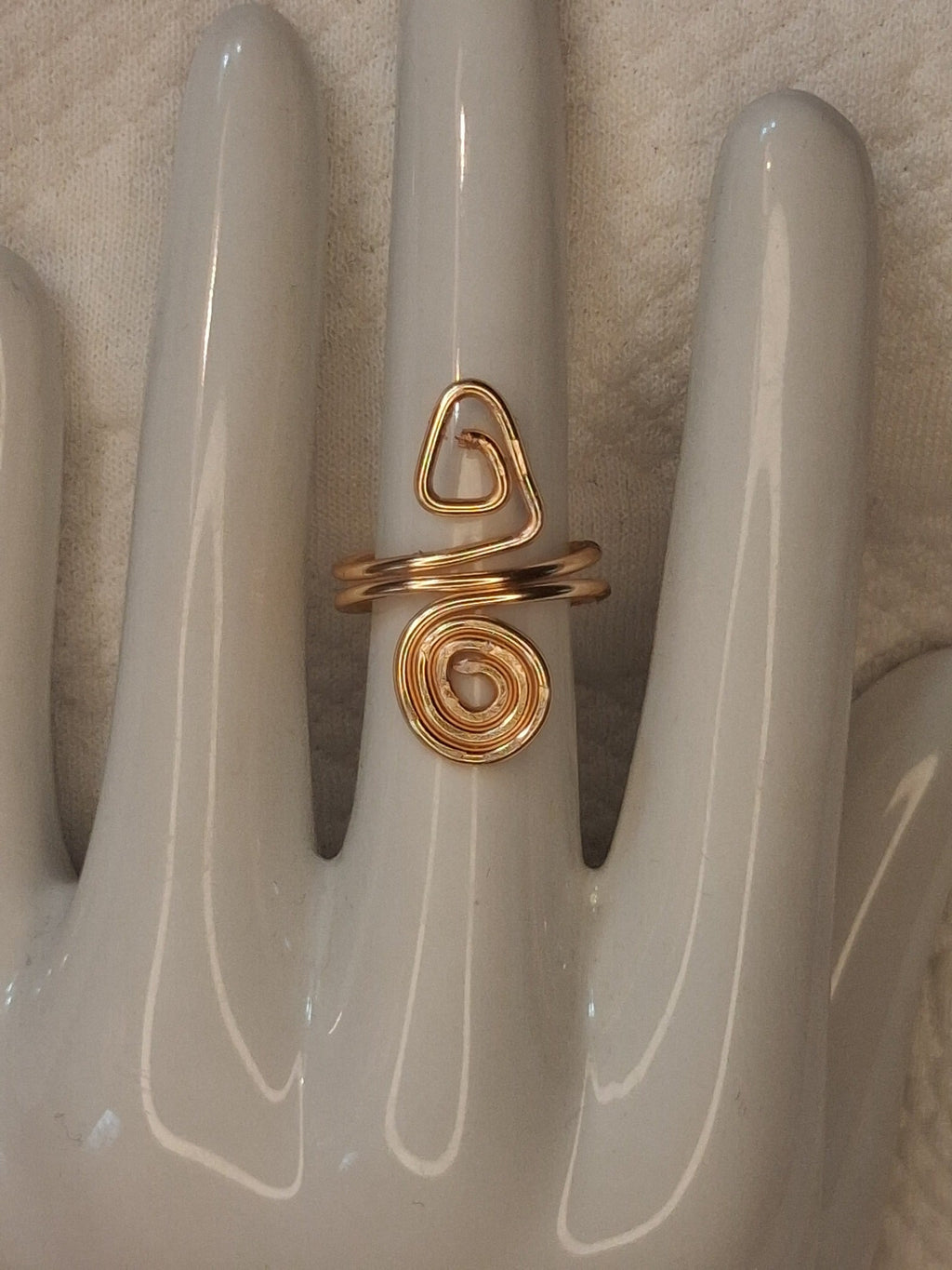 Gold 3 adjustable wire ring with a small triangular curl above a round spiral, displayed on a white ceramic jewelry hand.