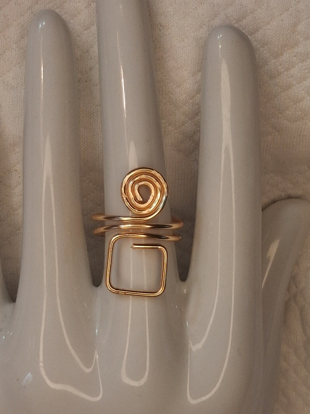 Gold 4 adjustable wire ring with a round spiral above an open square loop, displayed on a white ceramic jewelry hand.