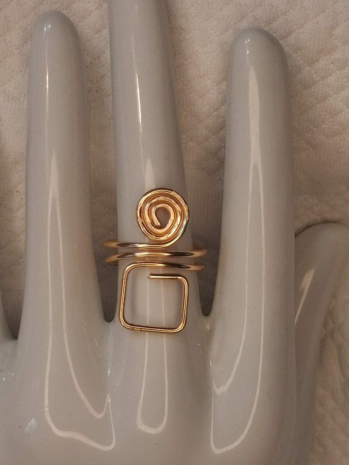 Gold 4 adjustable wire ring with a round spiral above an open square loop, displayed on a white ceramic jewelry hand.