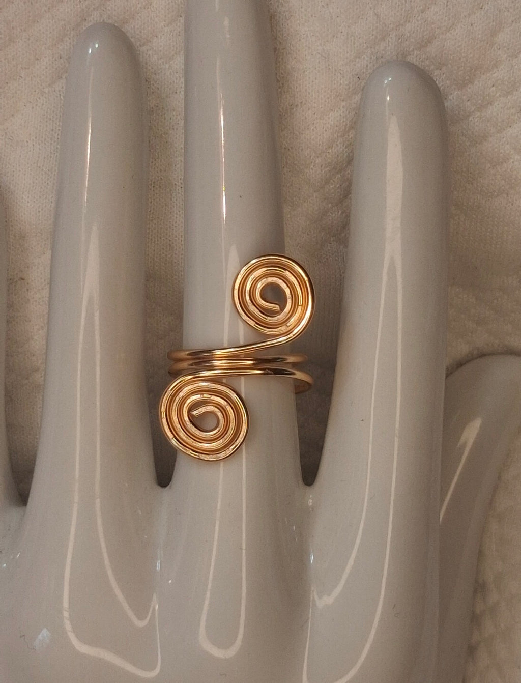 Gold 6 adjustable wire ring with two large round spiral ends on a white ceramic hand display.