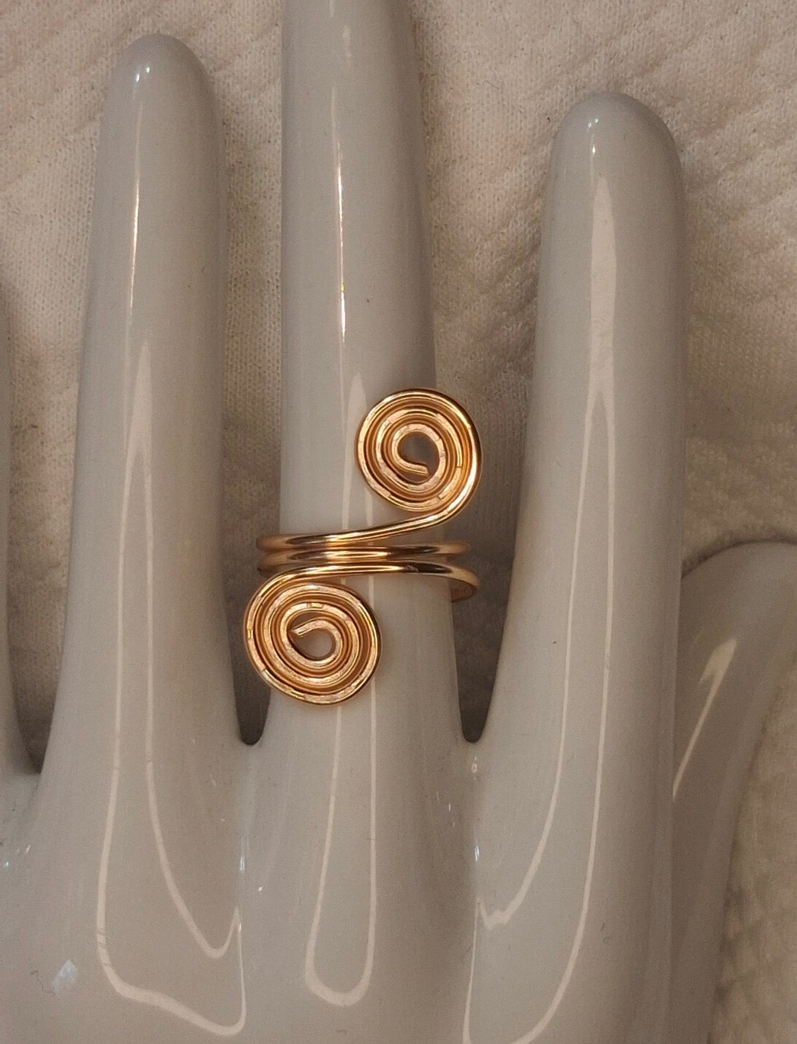 Gold 6 adjustable wire ring with two large round spiral ends on a white ceramic hand display.