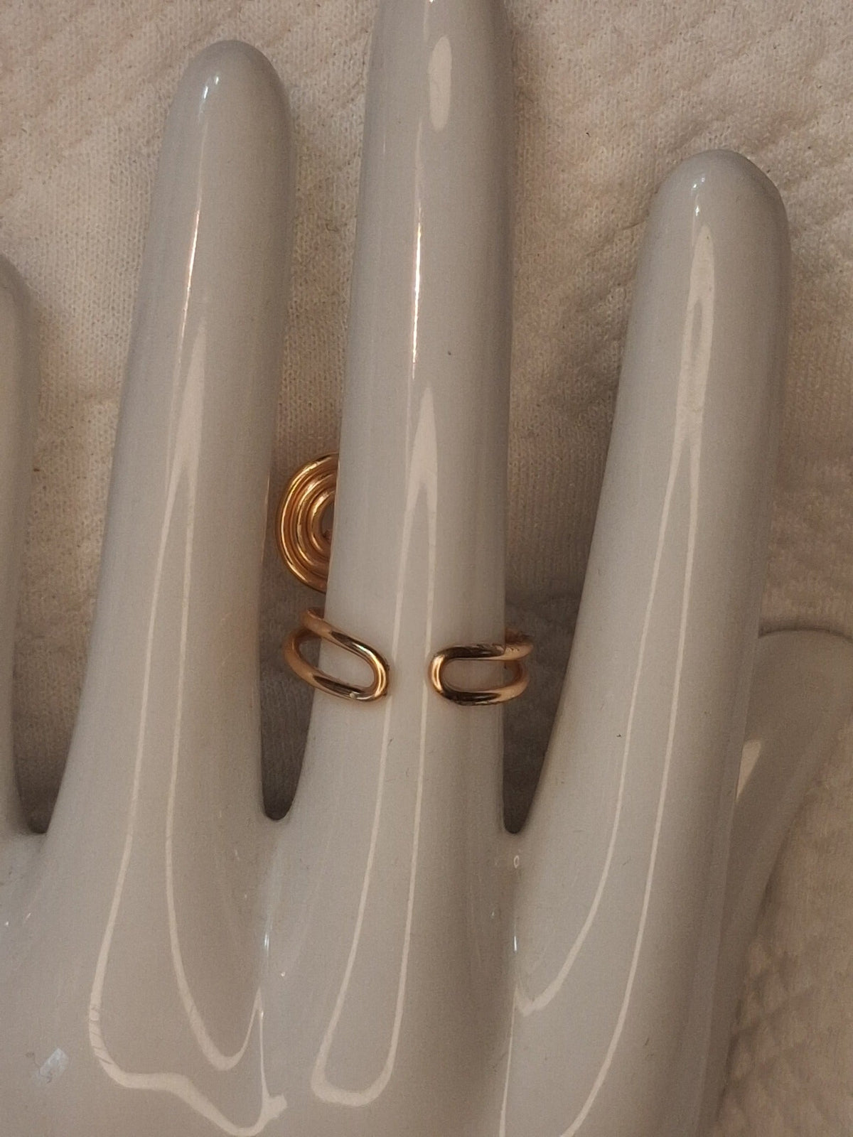 Shared back view of a gold wire ring showing the open adjustable band with folded rounded ends on a white ceramic jewelry hand.