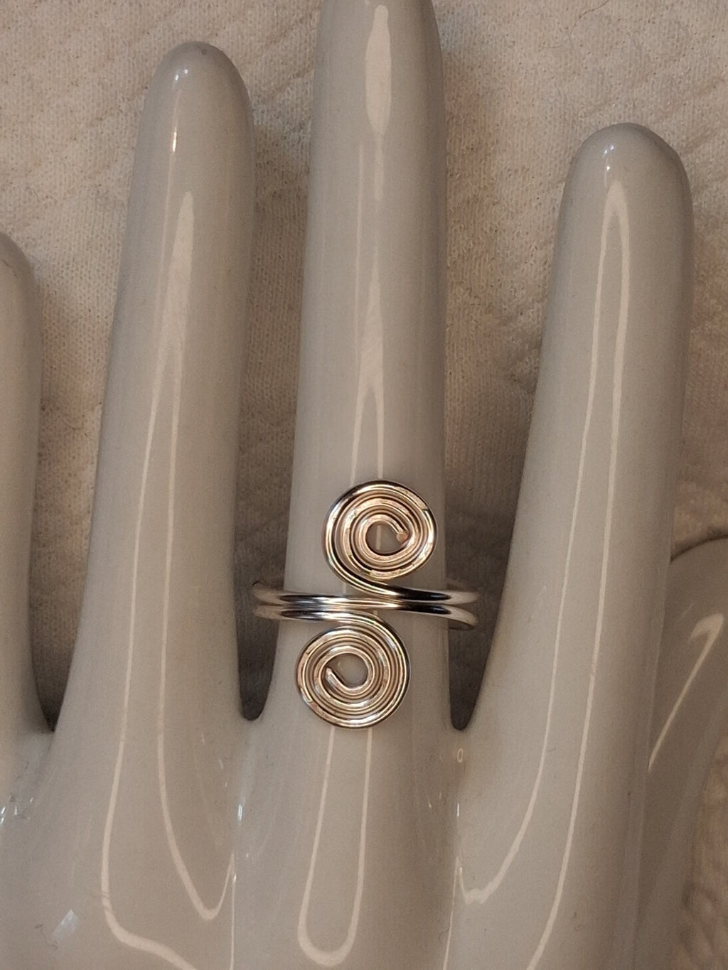 Silver adjustable wire ring 1 with two round spiral ends on a white jewelry display.