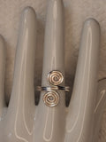Silver adjustable wire ring 1 with two round spiral ends on a white jewelry display.