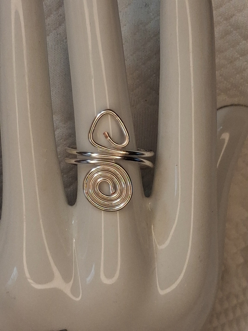 Silver adjustable wire ring 3 with an open triangular loop and a round spiral on a white jewelry display.