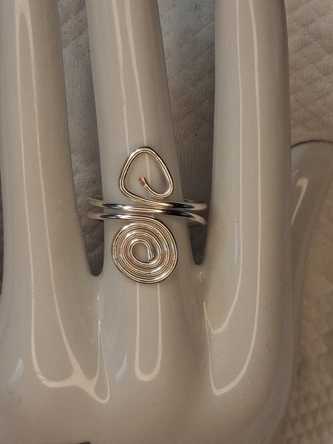 Silver adjustable wire ring 3 with an open triangular loop and a round spiral on a white jewelry display.