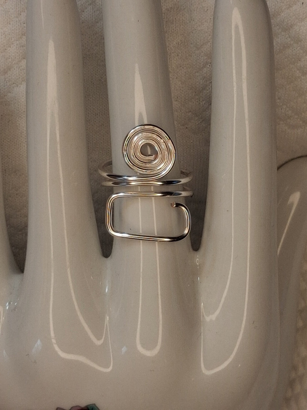 Silver adjustable wire ring 4 with a round spiral and an open rectangular loop on a white jewelry display.