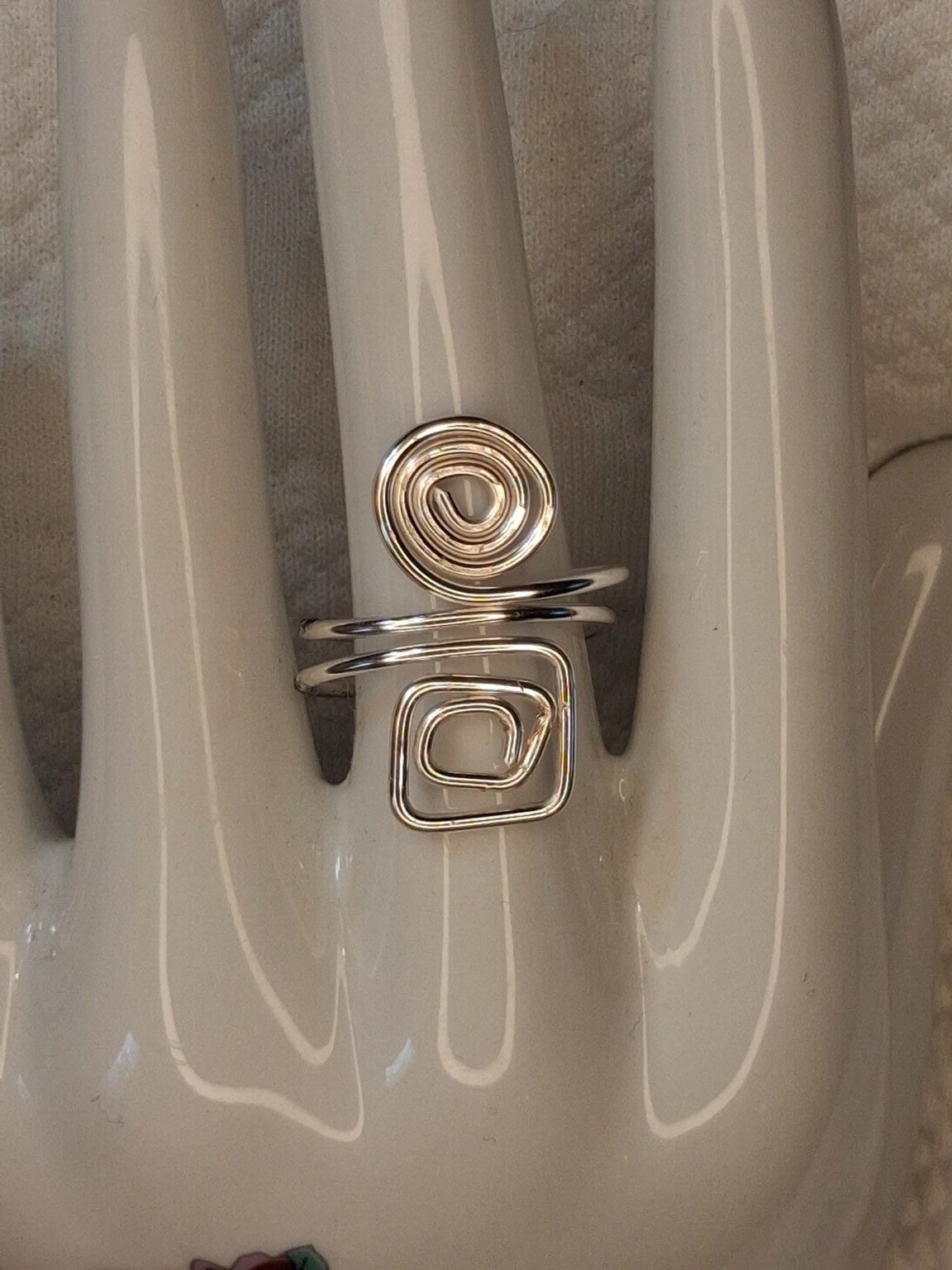 Silver adjustable wire ring 5 with a round spiral and a square spiral on a white jewelry display.