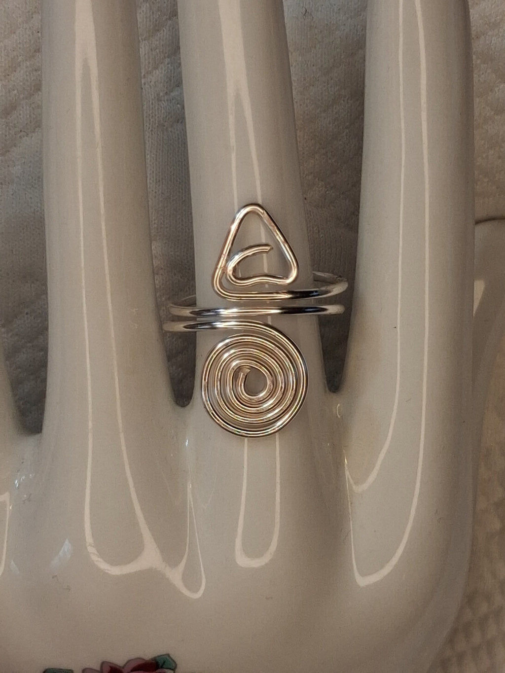 Silver adjustable wire ring 7 with a triangular curl and a round spiral on a white jewelry display.