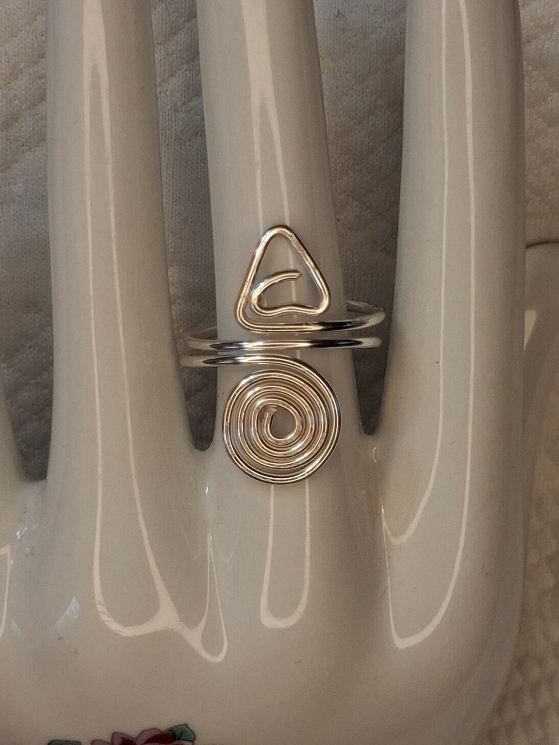 Silver adjustable wire ring 7 with a triangular curl and a round spiral on a white jewelry display.