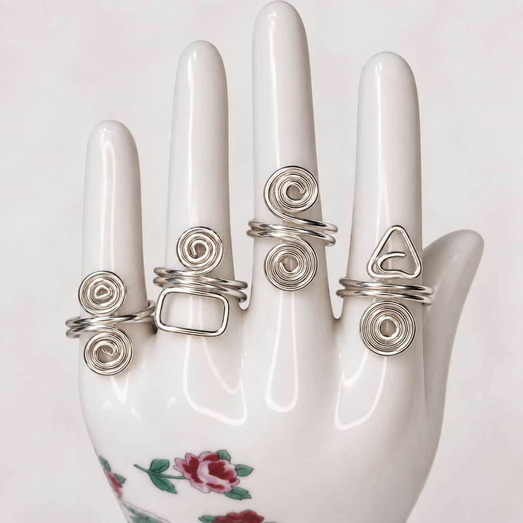 Four adjustable silver wire rings with spiral and geometric designs displayed on a white floral ceramic hand. Rings sold individually.