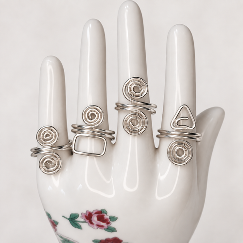 Four adjustable silver wire rings with spiral and geometric designs displayed on a white floral ceramic hand. Rings sold individually.