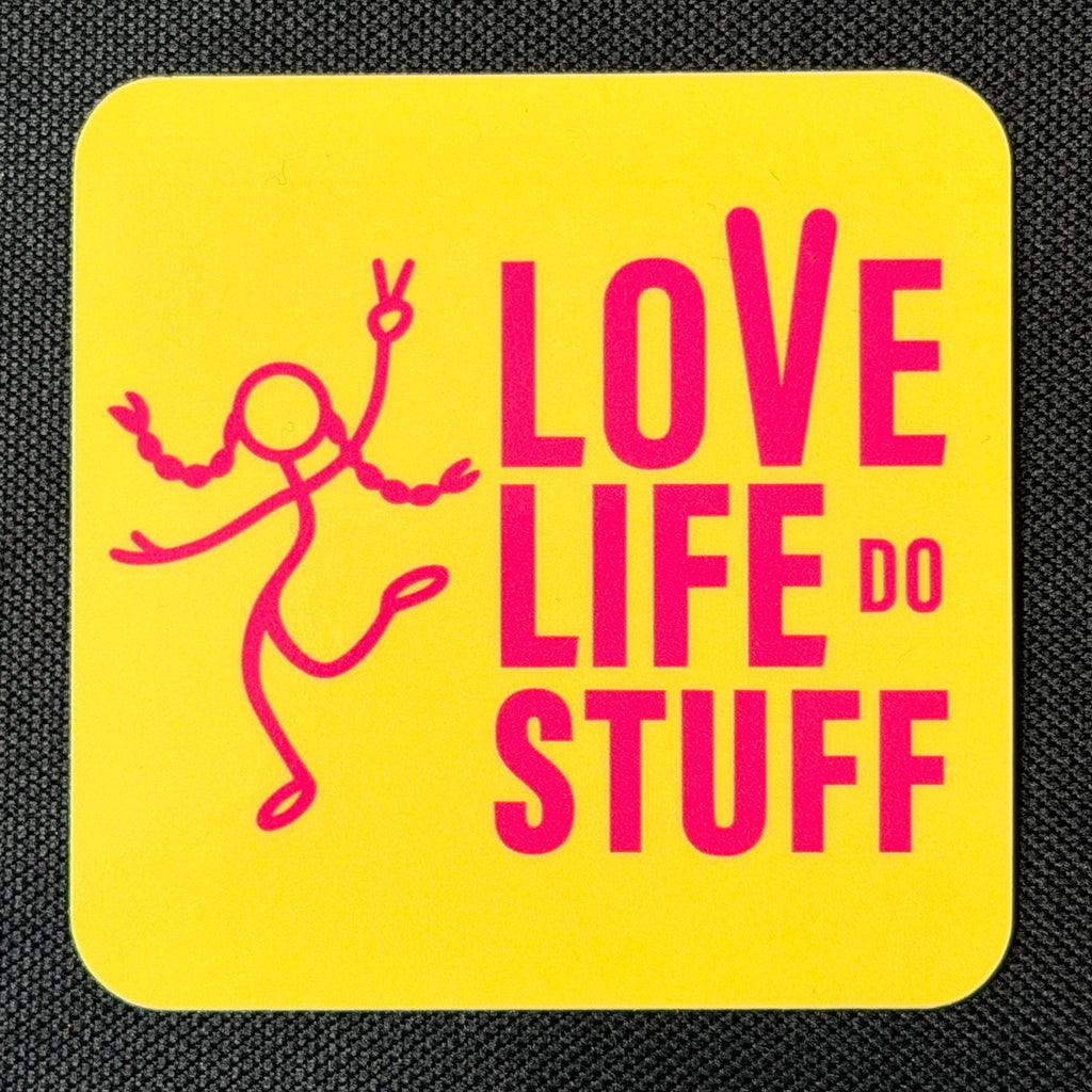 Pink on Yellow Stick Figure vinyl sticker on black fabric, with hot pink Love Life Do Stuff lettering and a dancing stick figure on a bright yellow rounded square.