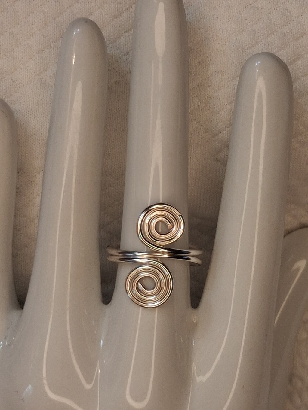 Silver 10 adjustable wire ring with two round spiral ends, shown on a white ceramic hand display.